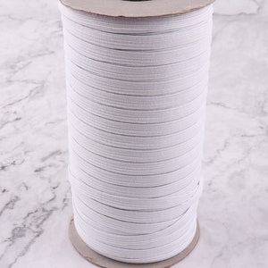 May include: A spool of white elastic cord, wound tightly on a cardboard core. The elastic is smooth and appears to be of good quality.