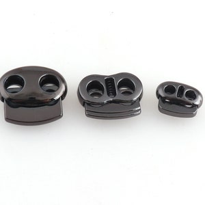 Puede incluir: Tres cierres de palanca de metal negro de diferentes tamaños. Los cierres tienen dos agujeros cada uno y se utilizan para asegurar cordones o correas.