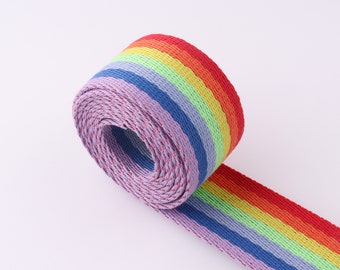 May include: A rainbow striped webbing with a purple and red trim. The webbing is rolled up and the end is laying flat.