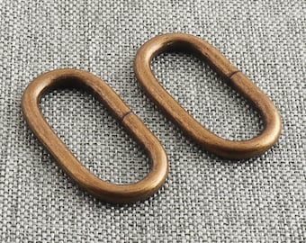 May include: Two oval-shaped, bronze-colored metal rings. The rings have a smooth, polished finish and a slight sheen. The rings are placed on a textured, gray fabric surface. The rings are likely used for jewelry making or crafting.