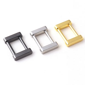 May include: Three metal D-ring clasps in black, silver, and gold. The rings are rectangular with rounded corners and have a smooth finish.