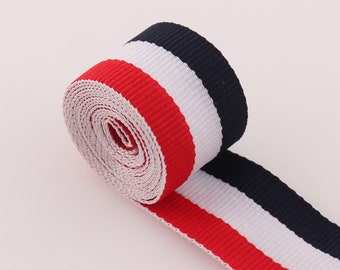 May include: Red, white, and navy blue striped ribbon. The ribbon is rolled up and the stripes are visible.