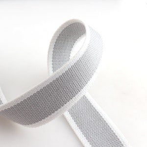 May include: A white and gray striped cotton webbing ribbon. The ribbon is woven with a subtle texture.