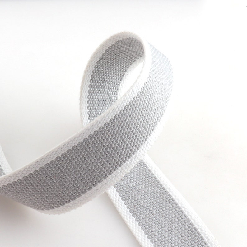 May include: A white and gray striped cotton webbing ribbon. The ribbon is woven with a subtle texture.