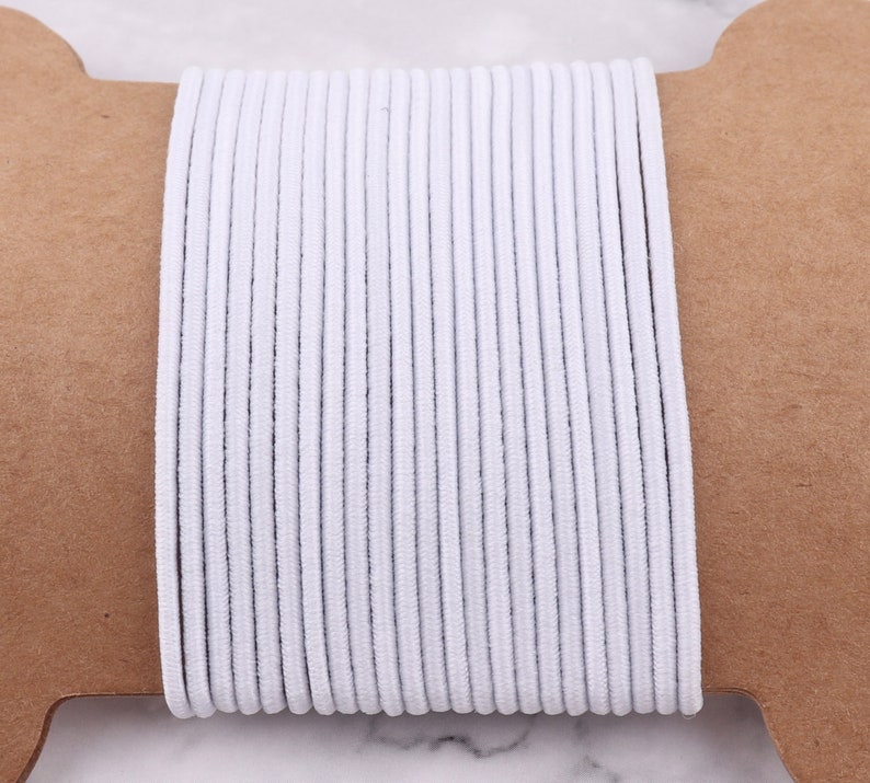 May include: A spool of white elastic cord, wound tightly and ready for use in crafting projects.