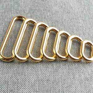 May include: A set of seven gold-toned metal oval rings of varying sizes. The rings are arranged in order of size, with the largest ring on the left and the smallest ring on the right.