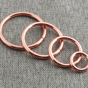 Op de afbeelding: Vier roosgoudkleurige metalen ringen in verschillende maten. De ringen zijn glad en glanzend.