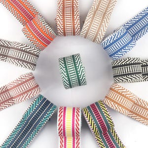 May include: Assortment of 12 colorful woven ribbon trims with chevron patterns. The ribbons are in various colors, including red, green, blue, brown, and white.