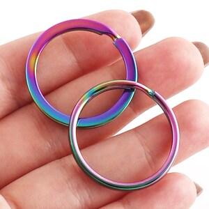 May include: Two iridescent key rings, one larger than the other, are shown in a hand. The key rings are a rainbow of colors, including purple, blue, green, and red.