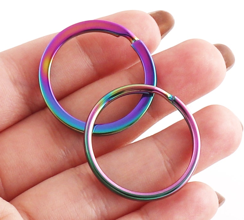 May include: Two iridescent key rings, one larger than the other, are shown in a hand. The key rings are a rainbow of colors, including purple, blue, green, and red.