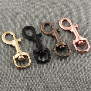 May include: Four metal swivel snap hooks in different finishes: gold, brass, black, and rose gold. The hooks are all the same size and shape, with a spring-loaded gate.