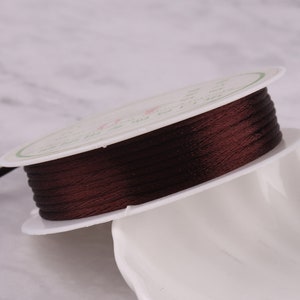 May include: A spool of brown waxed cord, wound on a white plastic spool. The cord is smooth and shiny.