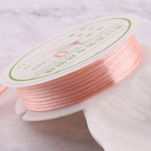 May include: A spool of peach-colored thread wound around a white plastic bobbin. The bobbin has a label with Japanese text.