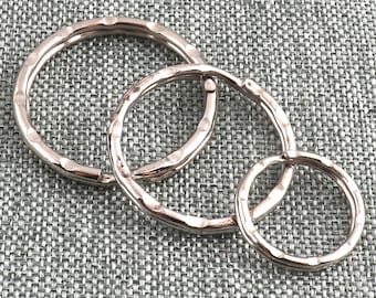 Könnte beinhalten: Drei silberne Schlüsselringe in verschiedenen Größen, jeweils mit einer gehämmerten Oberfläche. Die Ringe sind ineinander verschlungen und auf einer strukturierten grauen Oberfläche angeordnet.