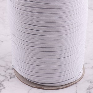 May include: A roll of white elastic cord, perfect for sewing projects. The cord is wound tightly on a cardboard tube.
