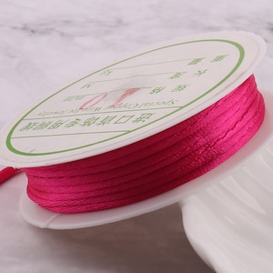 May include: A spool of bright pink satin cord, wound around a white plastic bobbin. The bobbin has a label with Chinese text and the words "Special Cord".