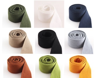 Könnte beinhalten: Sortiment aus 10 Baumwoll-Gurtbändern in verschiedenen Farben, darunter Grün, Beige, Schwarz, Grau, Orange und Braun. Jedes Band ist etwa 2,5 cm breit und hat eine gerippte Textur.