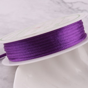 May include: A spool of purple waxed cord, wound around a white plastic spool. The cord is smooth and shiny.