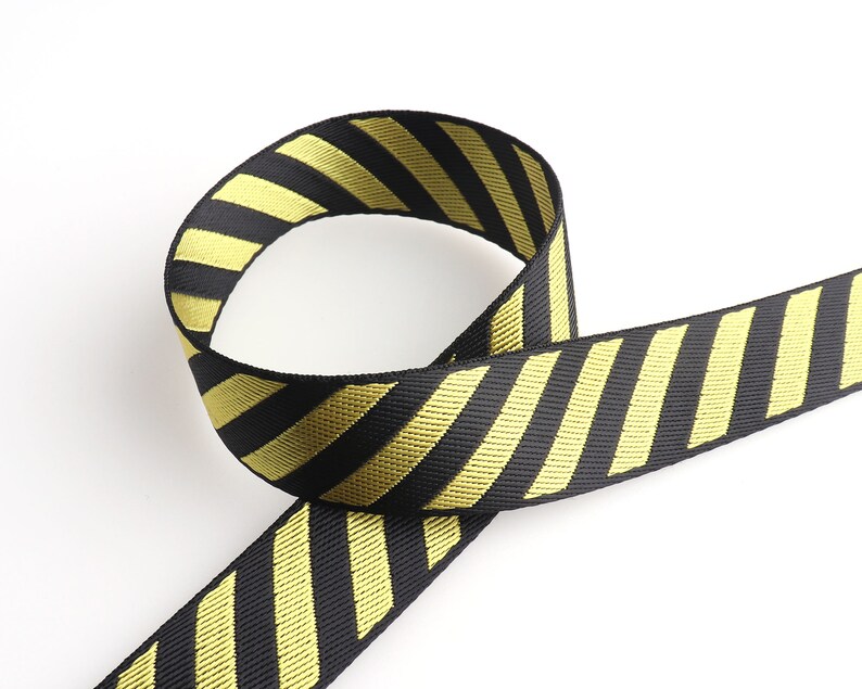 May include: Black and yellow striped ribbon with a diagonal pattern. The ribbon is folded in a loop.