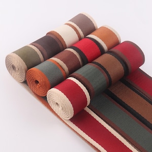 Puede incluir: Surtido de cinta de tela a rayas en varios colores, incluyendo marrón, rojo, beige y verde. La cinta está tejida con una textura sutil.