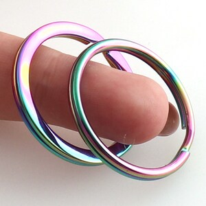May include: Two iridescent key rings, one slightly larger than the other, are shown stacked together. The rings are a rainbow of colors, including pink, purple, green, and blue.