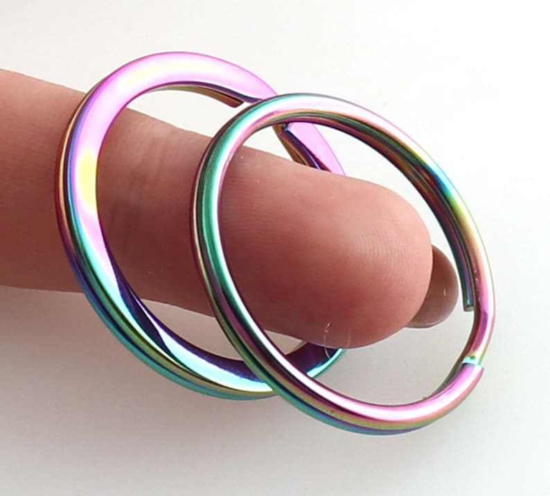 May include: Two iridescent key rings, one slightly larger than the other, are shown stacked together. The rings are a rainbow of colors, including pink, purple, green, and blue.
