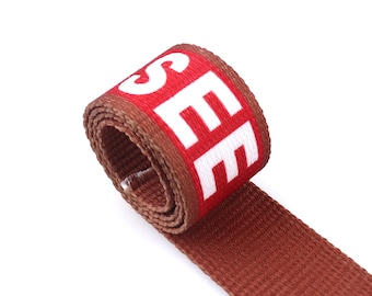 May include: Brown woven strap with the word "SEE" printed in white letters on a red background.