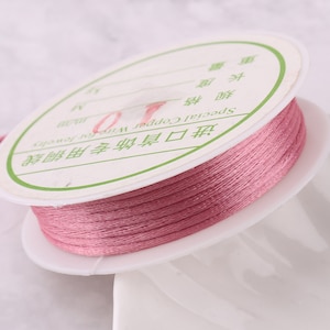 May include: A spool of pink waxed cord for jewelry making. The label reads "Special Copper Jewelry Waxed Cord for Jewelry Making".