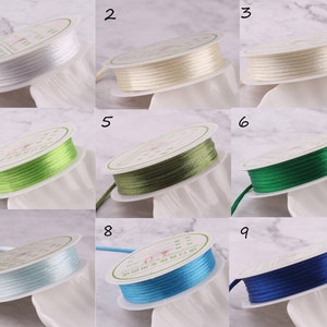 May include: Nine spools of satin cord in various colours, including white, cream, green, light blue, and blue. Each spool is wound with the cord and labelled with a number from 1 to 9.
