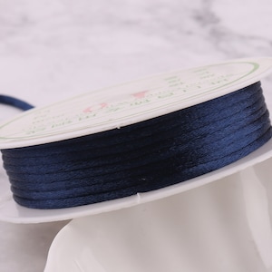 May include: A spool of dark blue waxed cord, wound around a white plastic spool with green text.