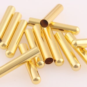 May include: A pile of gold-colored metal end caps. The end caps are cylindrical and have a rounded end. They are used to finish off the ends of cords or cables.