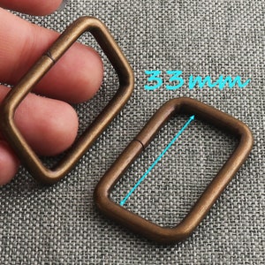 May include: Two antique gold-toned metal D-rings, one is slightly larger than the other. The larger ring measures 33 mm in length.