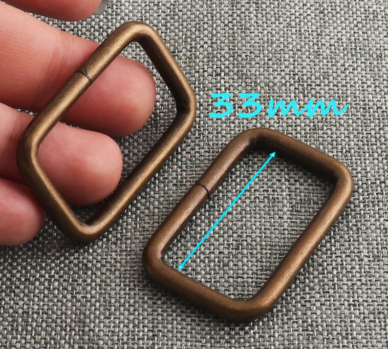 May include: Two antique gold-toned metal D-rings, one is slightly larger than the other. The larger ring measures 33 mm in length.