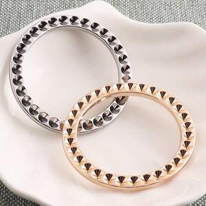 May include: Two silver and gold rings with a studded design. The rings are interlocked and have a circular shape.
