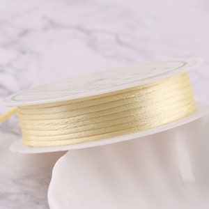 May include: A spool of pale yellow satin ribbon wound on a white cardboard spool.