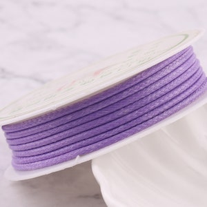 Peut inclure: Une bobine de cordon tressé violet, enroulée autour d'une bobine en carton blanc. Le cordon est lisse et a un léger brillant.
