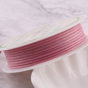 Peut inclure: Une bobine de cordon ciré rose, enroulée autour d'une bobine en plastique blanche. Le cordon mesure environ 1 mm d'épaisseur.