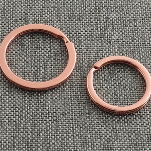 Könnte beinhalten: Zwei Schlüsselringe aus Roségold in verschiedenen Größen. Der größere Schlüsselring befindet sich links und der kleinere rechts.