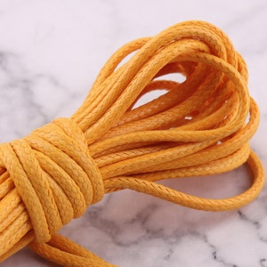 Peut inclure: Un paquet enroulé de corde jaune. La corde a une texture tressée et une couleur uniforme. La corde est probablement utilisée pour l'artisanat, le macramé ou d'autres projets de bricolage. Le fond est une surface semblable à du marbre.