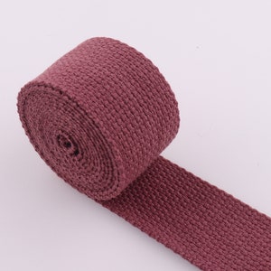 May include: A roll of maroon cotton webbing, a type of flat, woven fabric used for straps, belts, and other applications.