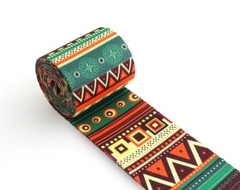 May include: A roll of green, orange, brown, and yellow patterned ribbon with geometric designs. The ribbon is rolled up and the end is unfurled.