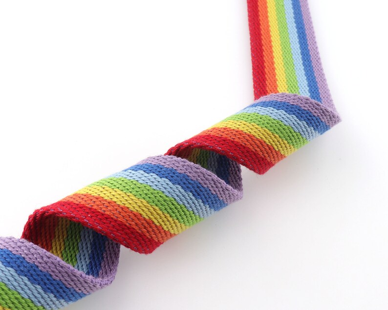 May include: A rainbow striped woven webbing with a purple, blue, green, yellow, orange, and red color scheme.