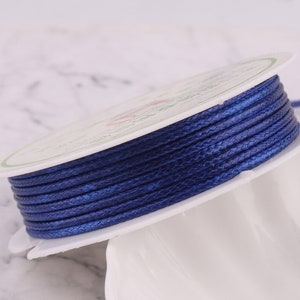 May include: A spool of dark blue braided cord, wound around a white cardboard spool.