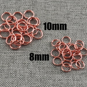 May include: Two piles of copper-coloured jump rings, one pile labelled "8mm" and the other labelled "10mm".