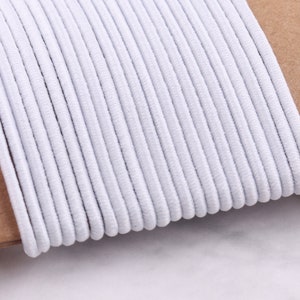 May include: A close-up of a spool of white elastic cord. The cord is wound tightly and is ready to be used for crafting or sewing projects.