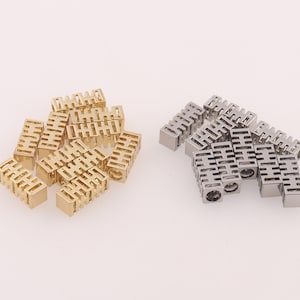 May include: A group of gold and silver metal charms with a repeating pattern. The charms are shaped like small rectangular blocks with a decorative design.