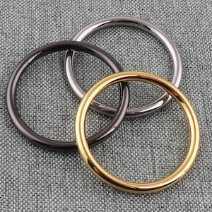 May include: Three metal rings, one gold, one silver, and one black, are interlocked and lying on a gray textured surface.