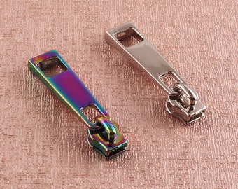 May include: Two metal zipper pulls, one silver and one iridescent. The silver zipper pull has a smooth finish, while the iridescent zipper pull has a rainbow finish.