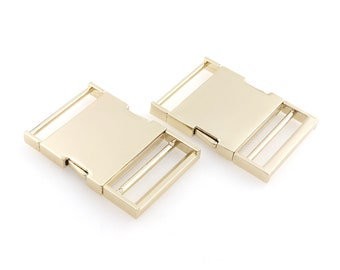 May include: Two gold-colored plastic side release buckles. The buckles are rectangular with a smooth surface and a single slider.