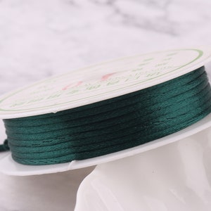 Può includere: Un rocchetto di cordoncino cerato verde scuro, avvolto su un rocchetto di plastica bianca con testo cinese stampato sull'etichetta.